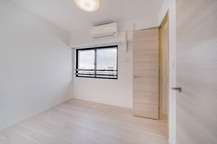 Unfurnished secondary bedroom with light wood flooring, white walls, a single window with a city view, and a light wood-paneled entrance door.