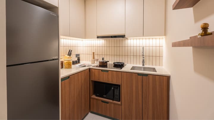 Corner view of the kitchenette with wood-grain and cream cabinets, a black refrigerator, and an integrated black microwave under the counter.