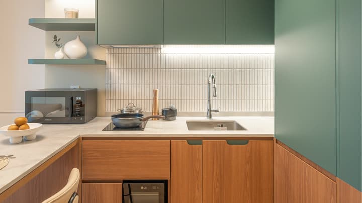 Detailed view of the kitchenette, featuring a stainless steel sink, a two-burner induction cooktop with a frying pan, and a backsplash of vertical white subway tiles, all set beneath green cabinets.