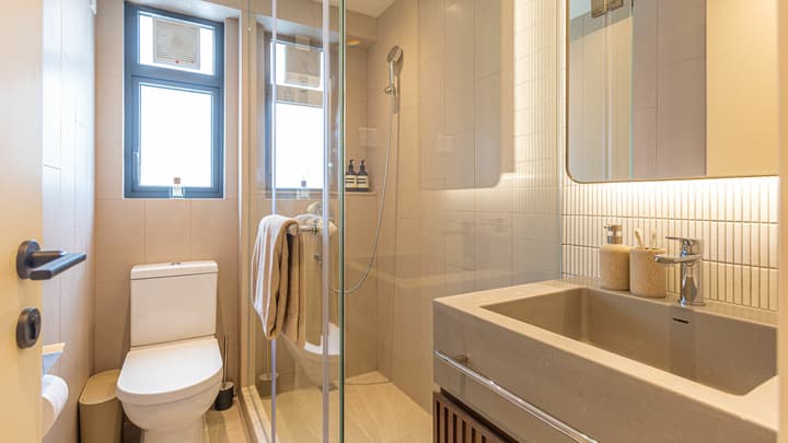 Contemporary bathroom with a concrete basin, glass shower enclosure, a toilet, and light-colored vertical subway tiles under backlighting.