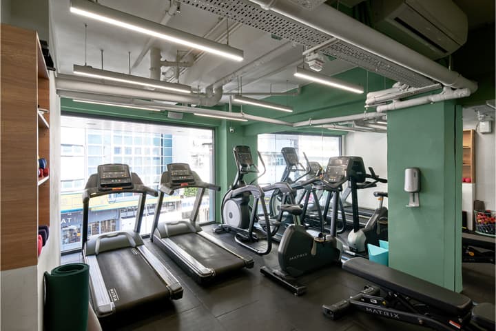 An on-site fitness center with bright green accent walls, featuring several treadmills, elliptical machines, and exposed ductwork on the ceiling.