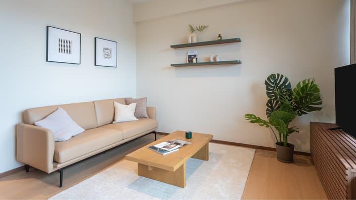 Modern living room with a tan leather sofa, wood coffee table on a white rug, and wall-mounted shelving with decor.
