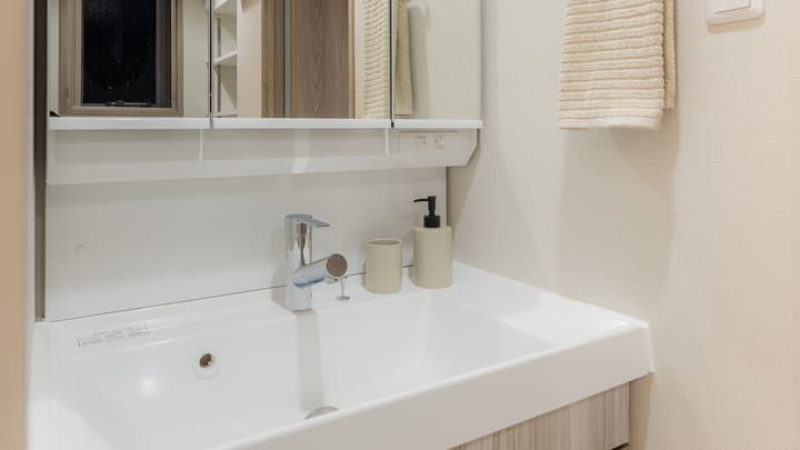 Bathroom vanity area with a white rectangular sink, modern faucet, mirrored medicine cabinet above, and light beige textured wallpaper in Monzennakacho.