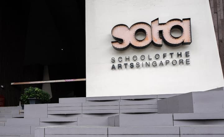 Close-up of the entrance sign for SOTA (School of the Arts Singapore), with large steps leading up to the main dark entrance area.