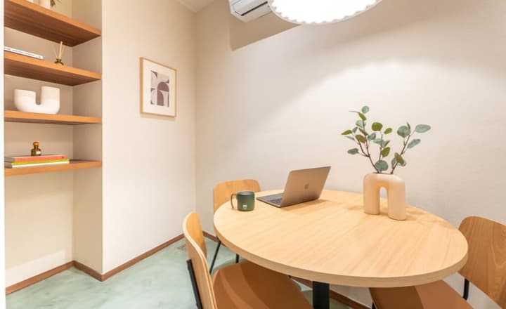 Cozy, small meeting room with a light wood round table, warm tan chairs, and built-in shelving with decorative items.