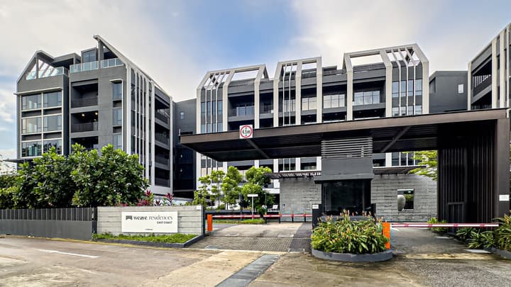 The modern, dark grey facade and main entrance gate of the Weave Residences East Coast apartment complex.