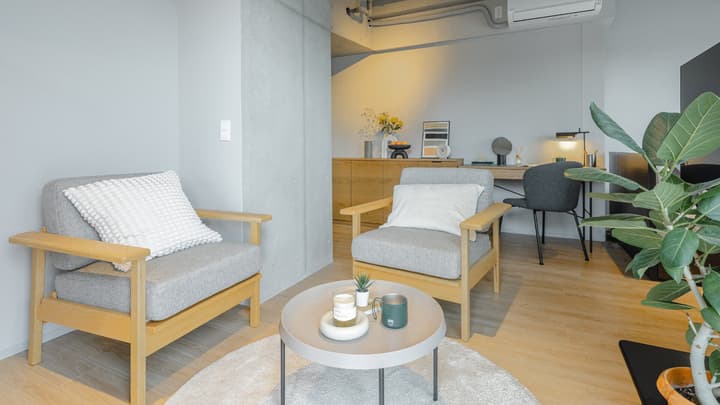 Close-up of the lounge area with two gray and wood armchairs, a white circular rug, and a light gray round coffee table with drinks and remote control.