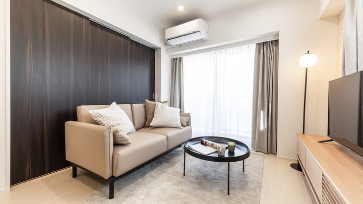 Room Type GalleryaLiving room focused on the neutral sofa, dark accent wall with sliding door panels, an air conditioning unit, and sheer and blackout curtains over the sliding door to the balcony.