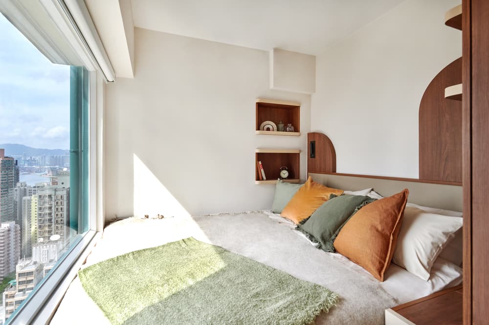 Cozy, modern bedroom featuring a built-in platform bed, warm wooden accents, and a floor-to-ceiling window offering a panoramic city and harbor view.