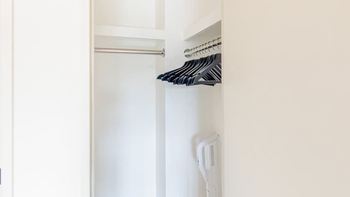 View inside the walk-in closet with a metal hanging rod, shelves, black hangers, and a stick vacuum cleaner stored against the wall.
