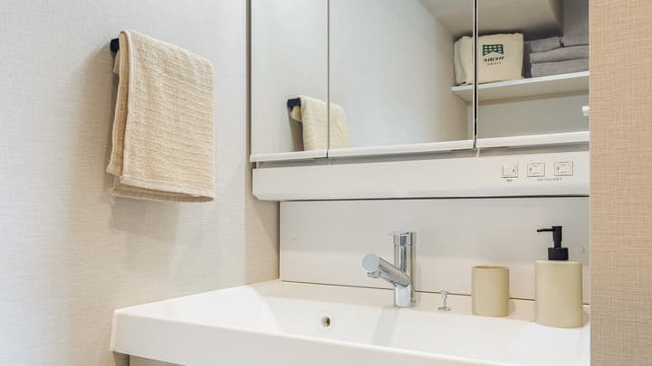 Close-up of the modern bathroom vanity with a white sink, chrome faucet, hand towel on a rack, and a mirrored cabinet above for storage.