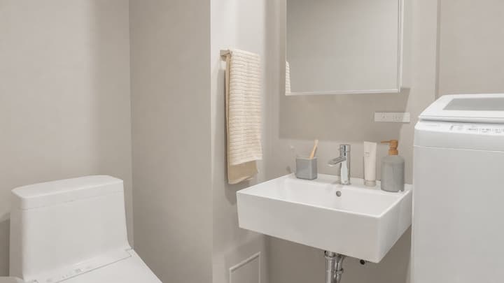 Bathroom area showing a modern square sink, a wall-mounted mirrored cabinet, a toilet, and a white washing machine to the right.