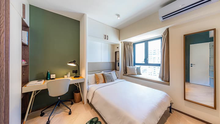Flexible room set up as a guest bedroom with a queen bed, built-in storage, a compact desk against a deep green accent wall, and a full-length mirror.