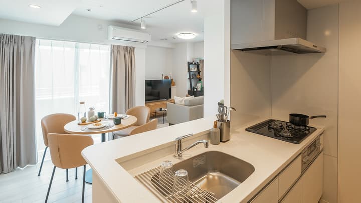 View of the kitchen counter with a sink and cooktop in the foreground, looking over the dining area and into the open-concept living room with a sofa and television.