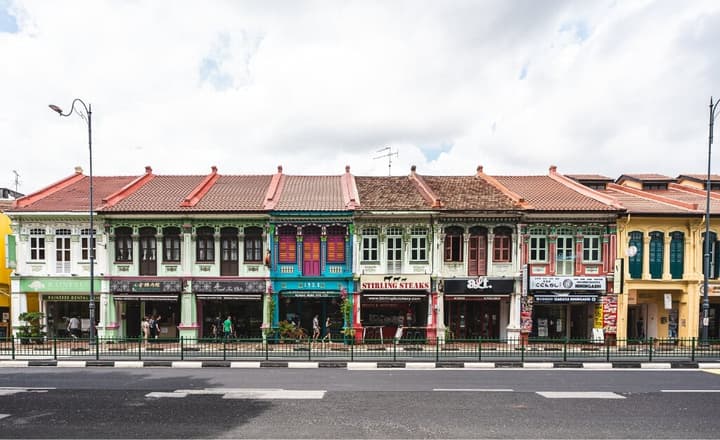A wide view of a street lined with beautifully preserved and brightly colored traditional Peranakan shophouses in the Katong neighborhood.