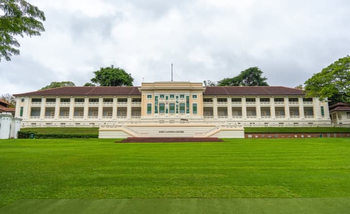 Historic Fort Canning Centre building with grand, colonial-era architecture, viewed from a distance across a wide, expansive green lawn.