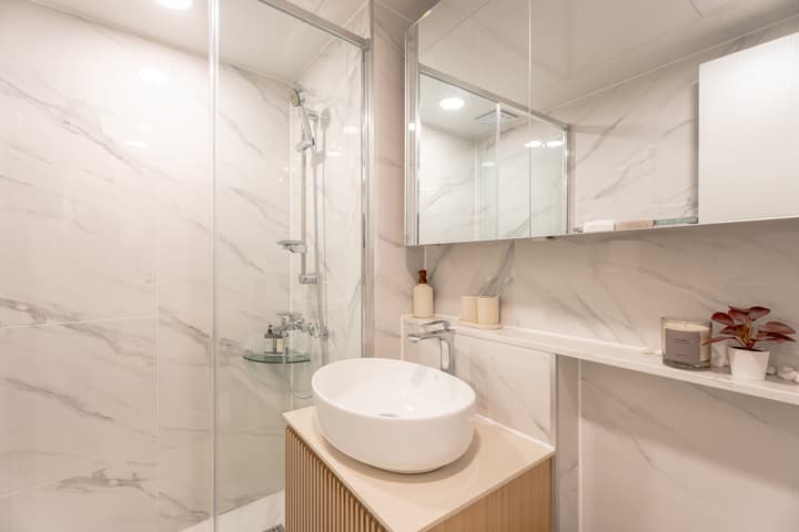 Modern bathroom with floor-to-ceiling marble-effect tiles, a glass-enclosed shower, a round vessel sink on a wood-slat vanity, and a mirrored medicine cabinet.