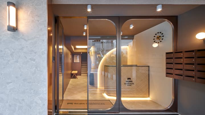 The stylish, modern entrance and lobby of Weave Residences with curved glass doors, a reception desk, and a wall of residential mailboxes.