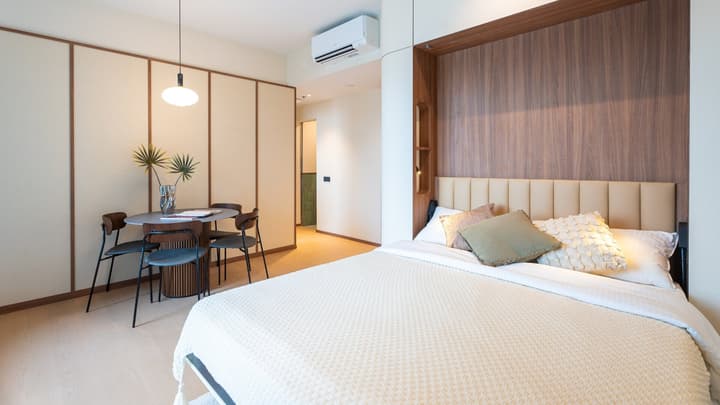 Full view of the bedroom and dining area, showing the bed set up against a wood accent wall, a round dining table, and neutral sliding partitions.