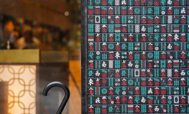 Close-up of a decorative wall made of mahjong tiles in black, white, red, and teal, with a black metal railing curving in the foreground.