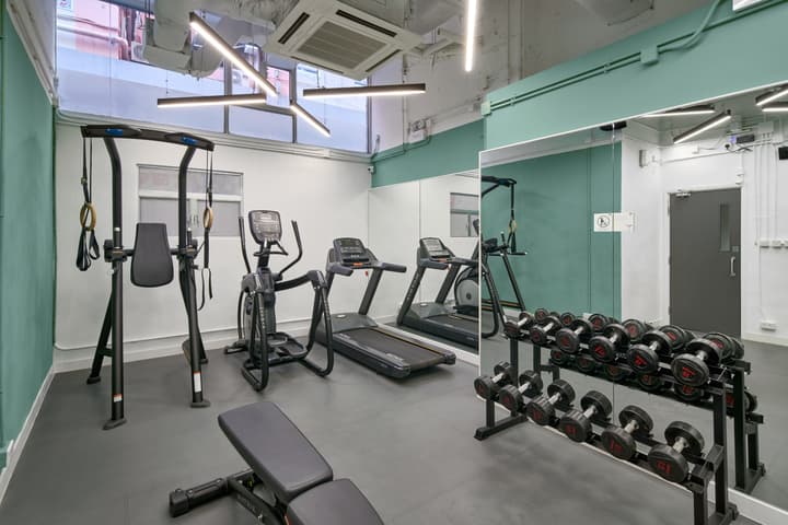 Modern, well-lit residential gym featuring two treadmills, an elliptical machine, a weight bench, and a rack of dumbbells, set against white and mint-green walls with large mirrors.