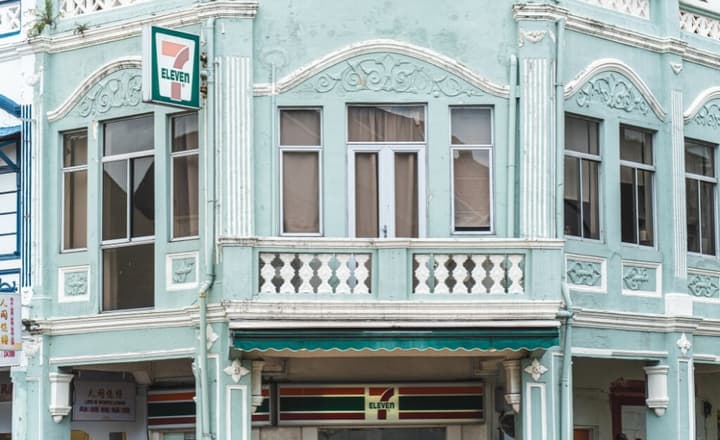 Detailed close-up of a traditional two-story shophouse facade painted mint green, with decorative railings and a 7-Eleven convenience store sign.