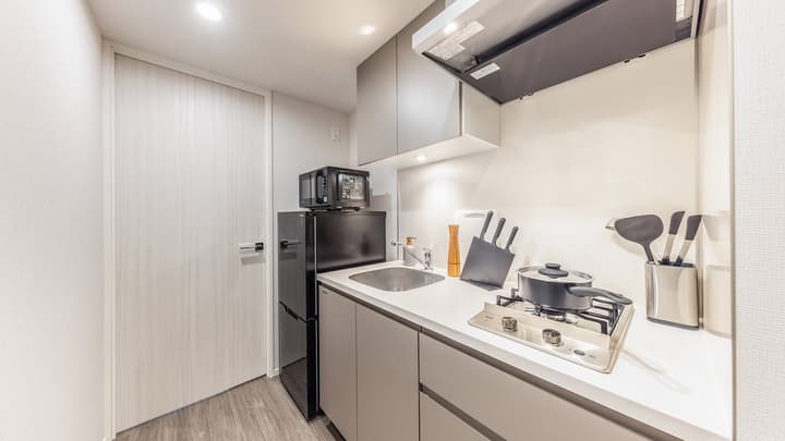 View of a compact, modern kitchenette with light gray cabinets, a two-burner gas cooktop, a small sink, a black mini-fridge, and an overhead microwave.