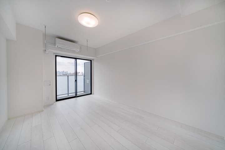 Unfurnished main living/sleeping room with white walls, light wood floors, an air conditioning unit, and a large sliding glass door leading to a balcony with a city view.