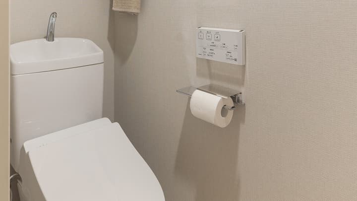 Close-up of a modern Japanese toilet with a built-in small sink for handwashing and an electronic bidet control panel on the wall.