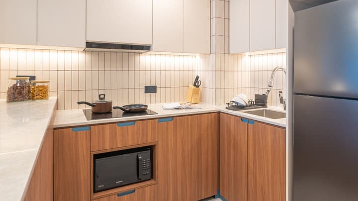 Kitchenette with light wood cabinets, an induction cooktop, a built-in microwave, and a white, vertical subway tile backsplash.