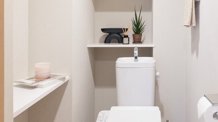 Clean toilet room with a washlet seat, a sink on top of the tank, and white floating shelves decorated with a potted plant and a diffuser in Monzennakacho.