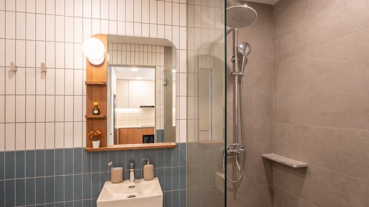 Modern bathroom with a rain shower, glass partition, a small basin sink, and a mirror set against a wall tiled in vertical white and horizontal blue subway tiles.
