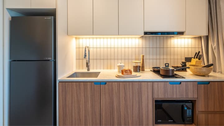 Compact kitchenette featuring wood lower cabinets, light upper cabinets, a dark integrated refrigerator, vertical beige backsplash tiles, and a built-in microwave.