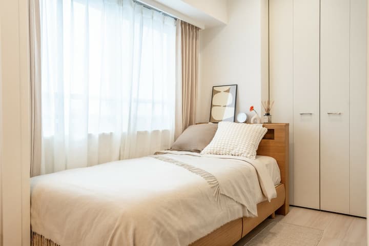 Cozy bedroom with a small wood bed frame, neutral-toned bedding, a decorative picture, and floor-to-ceiling storage closets.