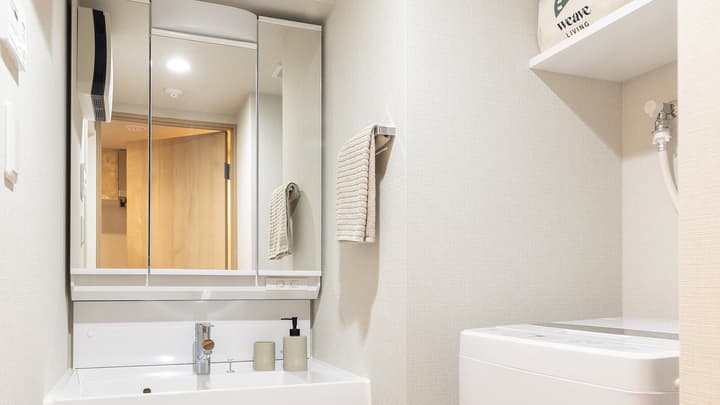 Bathroom vanity area with a white sink, mirrored medicine cabinet, towel rack, and a view of the adjacent white washing machine in Monzennakacho.