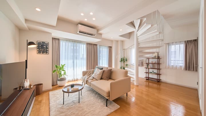 Spacious, open-plan living room with hardwood floors, a light beige sofa, a coffee table on a rug, and a prominent white spiral staircase to the loft.