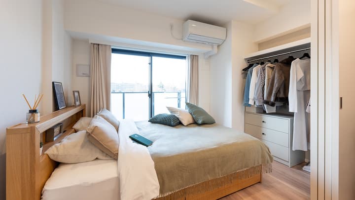 Spacious bedroom with a wooden bed frame, neutral bedding, a large sliding glass door to a balcony, and an open closet system.