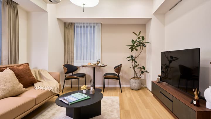 Bright, modern open-concept living and dining area with light-colored furniture, hardwood floors, and large windows.