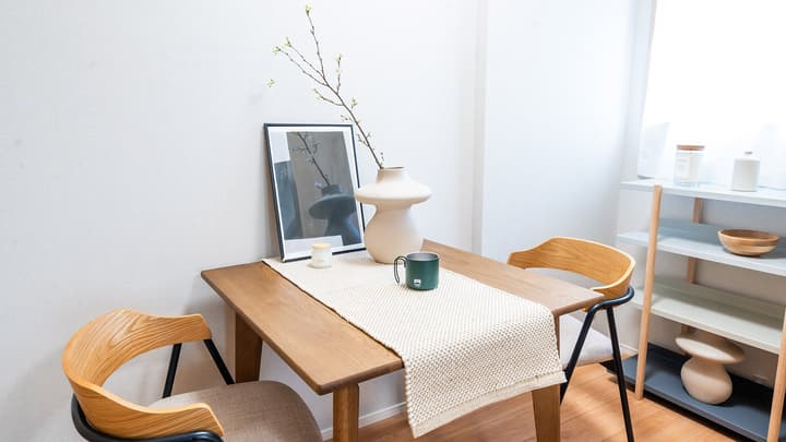 Close-up of a wooden dining table set with two modern chairs, featuring a white vase with decorative branches and a framed picture on the table in Monzennakacho.