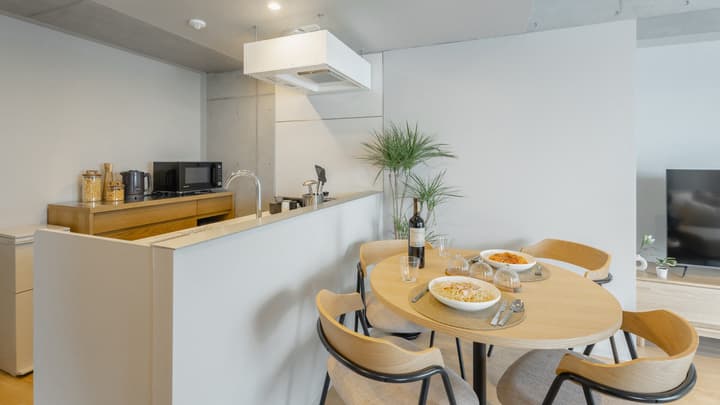 Close-up of the light wood dining table set for two with food and a bottle of wine, situated directly next to the kitchen counter and facing the living area.