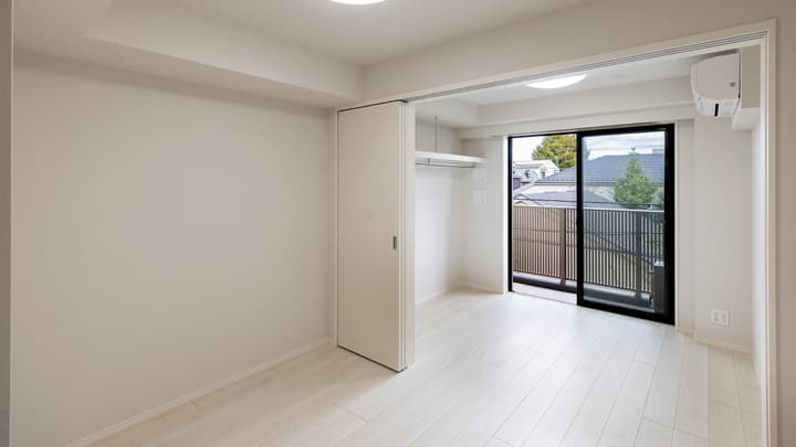 Unfurnished, brightly lit apartment room with light wood laminate flooring, a sliding closet door, and a large glass door leading to a balcony.