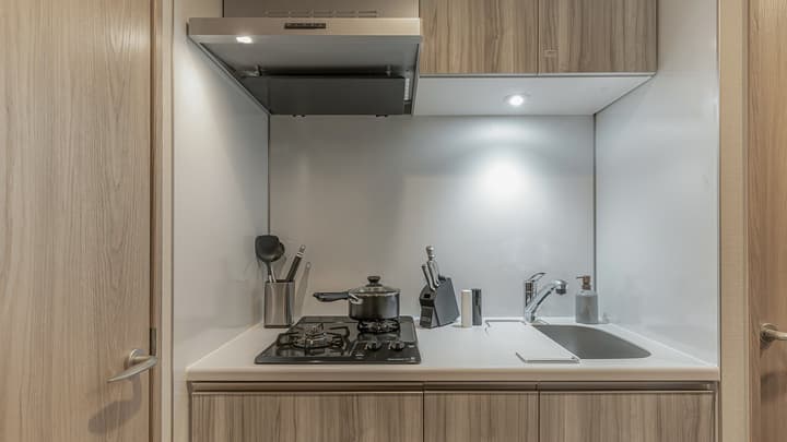 Compact kitchen area with gray-toned wood cabinets, white countertops, a black two-burner gas cooktop, a stainless steel sink, and a range hood in