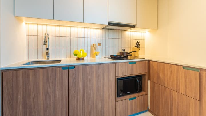 Compact kitchenette in a two-bedroom suite featuring walnut lower cabinets and light upper cabinets, an integrated microwave, and a vertical beige tiled backsplash.