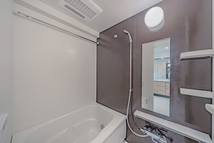 The bathtub/shower area with white and dark textured accent tiles, a silver shower fixture, and a mirror on the wall reflecting the opposite side of the bathroom.