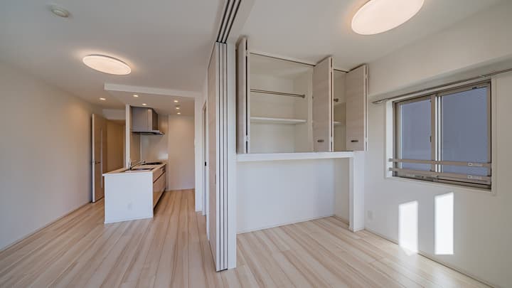 View of the main living area with light wood-style flooring, an open kitchen alcove in the back, and a closet/storage unit with open doors on the right.