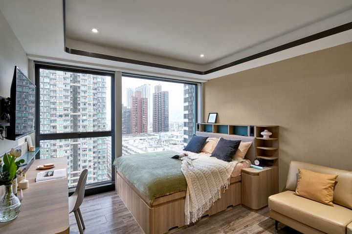Bright Queen Plus studio at Weave Studios – Kai Tak featuring a large window with city views, a cozy bed with storage, and a workspace.