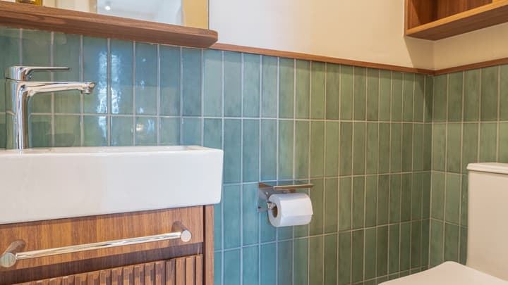 Detail of the bathroom area with a rectangular white sink, toilet, and walls tiled in vertical teal-green subway tiles.
