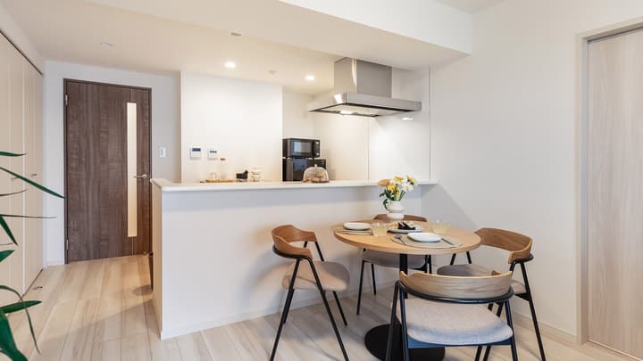View of the dining area in a large apartment, featuring a round wood table with four modern chairs and a white kitchen bar counter in the background.