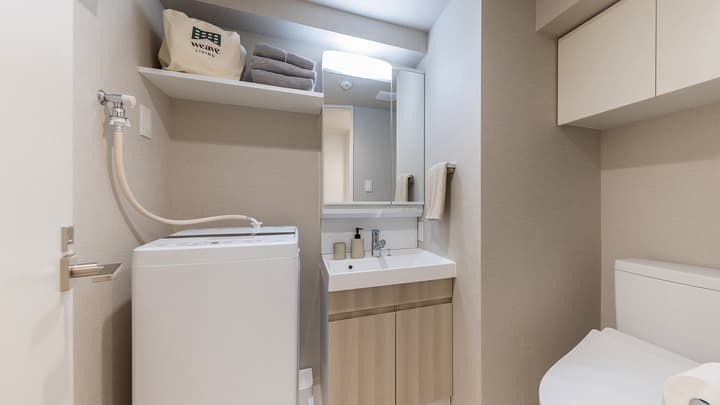 Laundry and washroom area featuring a white washing machine, small vanity sink, storage shelf, and a modern toilet.