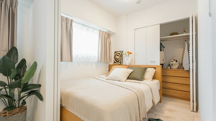 Bedroom with a wooden double bed and a sliding door closet opened to show a wooden chest of drawers and hanging clothes inside, next to a window.